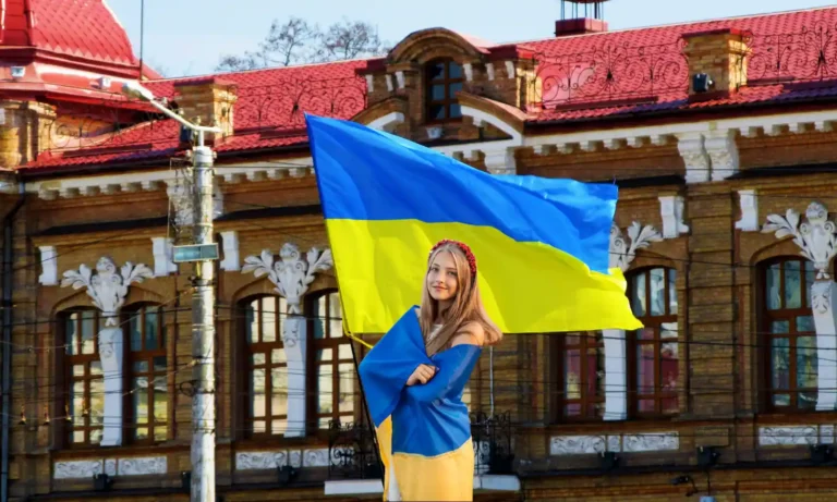 Una propiedad en Ucrania con una niña envuelta en una bandera ucraniana y la bandera del país ondeando.